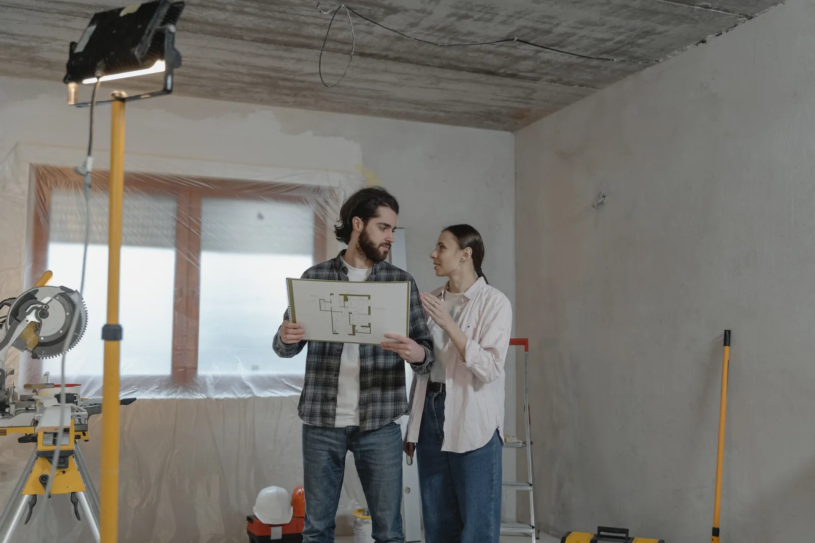 Couple étudiant un plan dans une pièce en cours de rénovation pour préparer les travaux de la maison