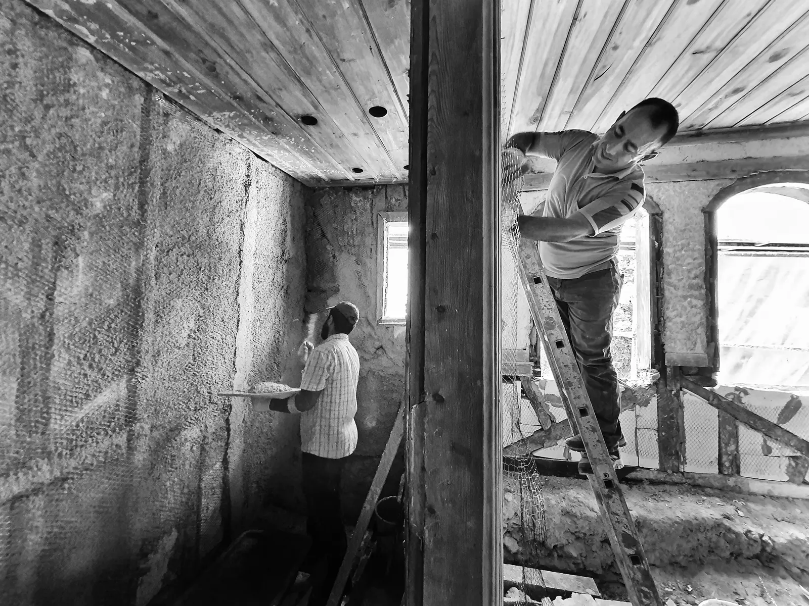 Deux ouvriers appliquant un enduit au plafond d'une pièce en rénovation, étape de second œuvre